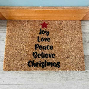 Doormat that has words in the shape of a Christmas tree with a red star on top. The words are Joy, Love, Peace, Believe, Christmas. 
